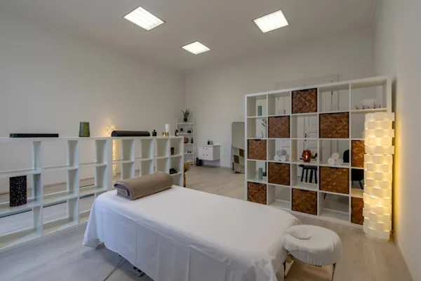 Heller Behandlungsraum mit weißer Massageliege und Handtuchregalen
