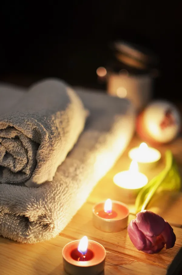 Gerollte Spa-Handtücher, Teelichter und eine lila Tulpe auf Holz