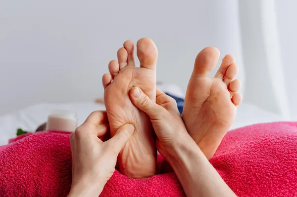 Nahaufnahme einer Fußmassage auf rosa Handtuch mit Creme daneben