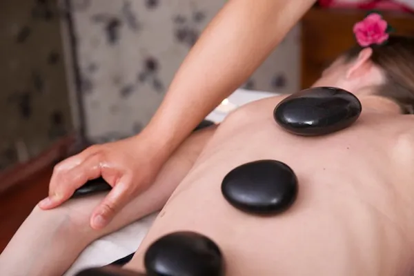 Hot-Stone-Massage mit schwarzen Steinen entlang des Rückens